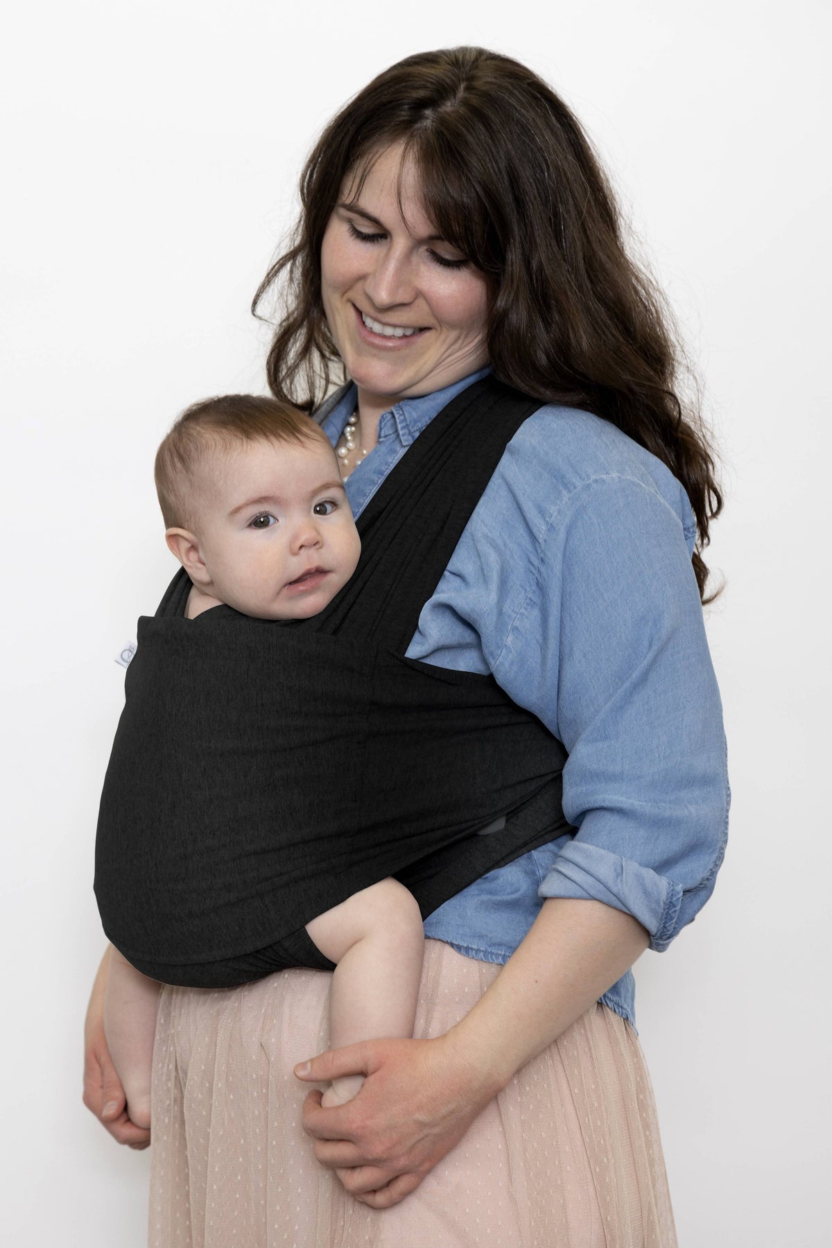 Woman holding a baby in a black carrier against a white background