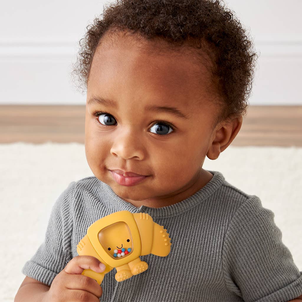 Child holding a yellow teether with a smiling face, wearing a gray sweater.