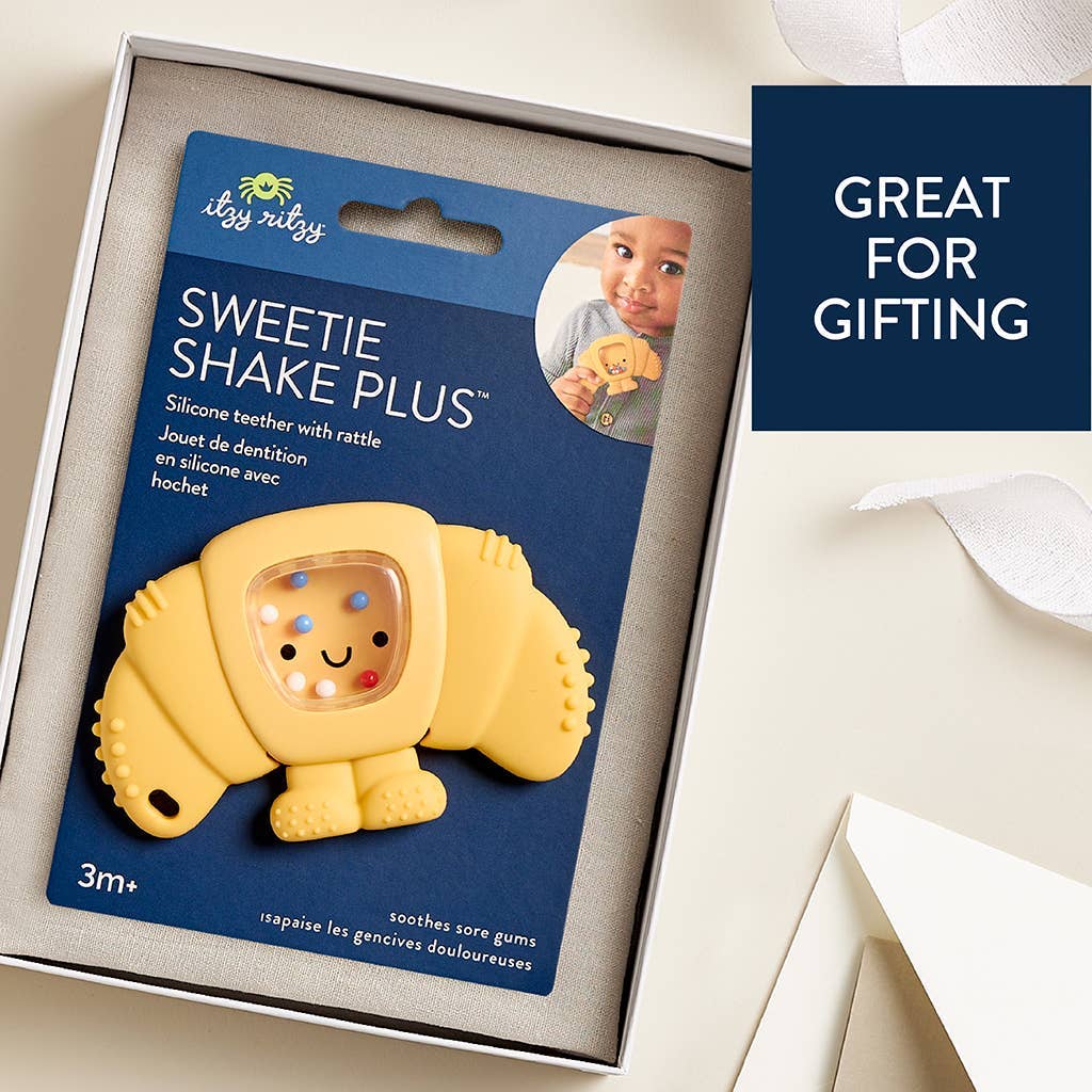 Yellow croissant-shaped silicone teether with packaging on a white surface