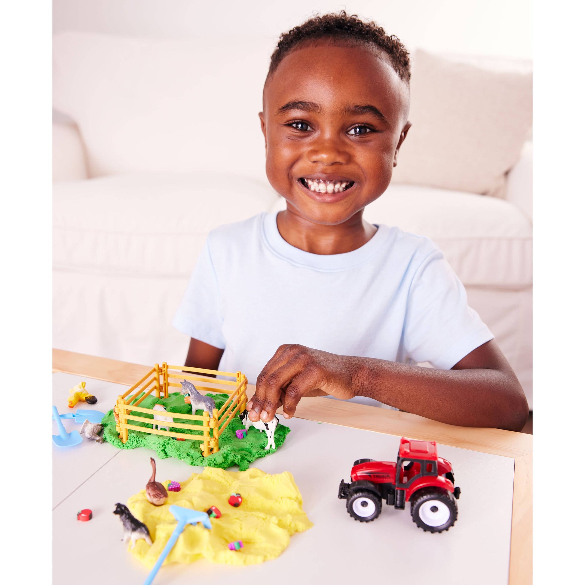 Child playing with farm toys including a red tractor and animal figures on a table.