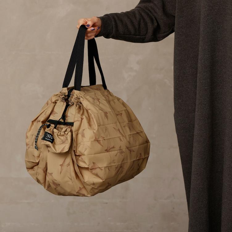 Person holding a beige drawstring bag against a neutral background