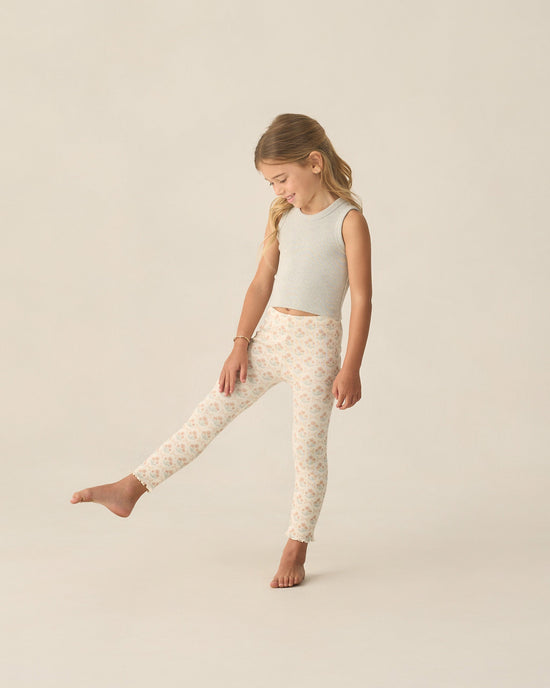 Young girl wearing a light gray sleeveless top and patterned leggings on a beige background